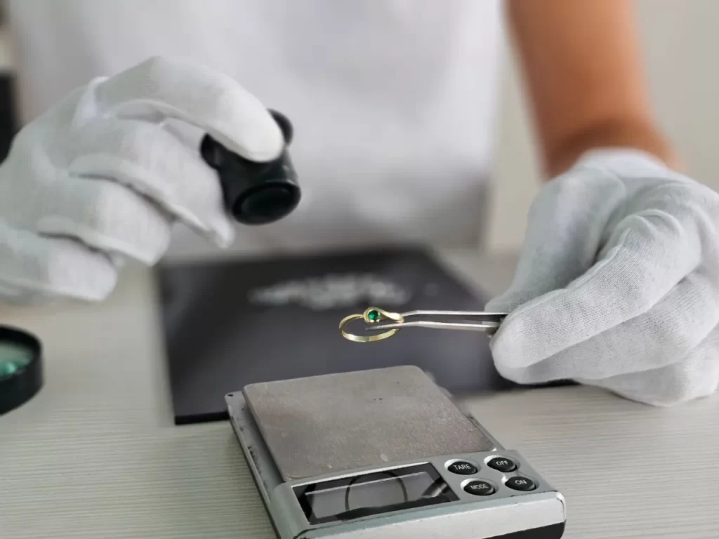 person in gloves examining a ring with a loupe over a scale
