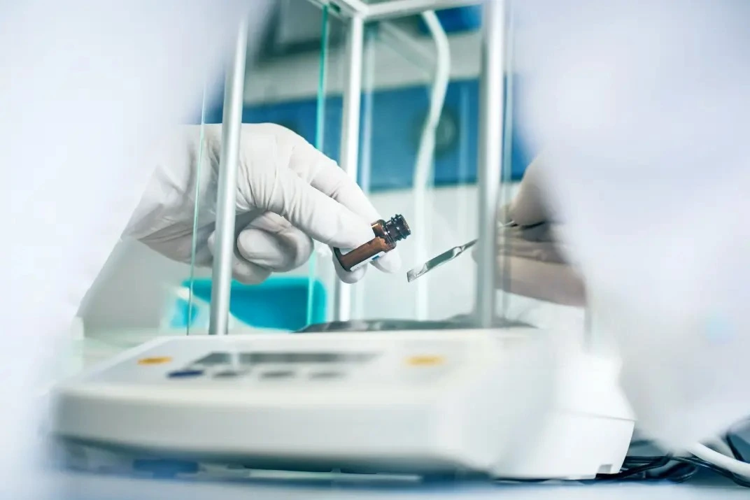wearing white gloves adding powder to analytical balance