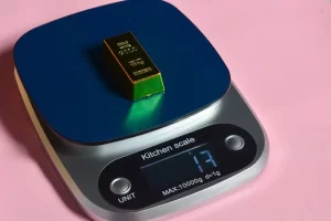 A gold bar on a digital kitchen scale, which displays "13" and has a maximum capacity of 1000g with a 1g divisionA gold bar on a digital kitchen scale, which displays "13" and has a maximum capacity of 1000g with a 1g division