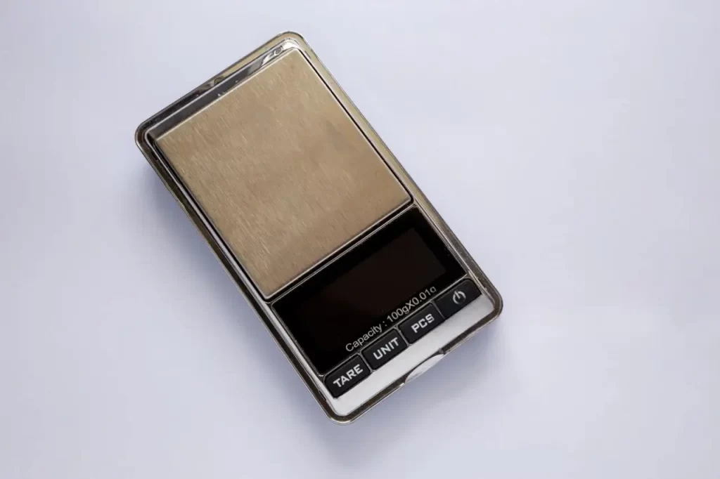 Digital pocket scale. Display shows capacity: 100g x 0.01g, with buttons for 'Tare', 'Unit' and 'Pieces'