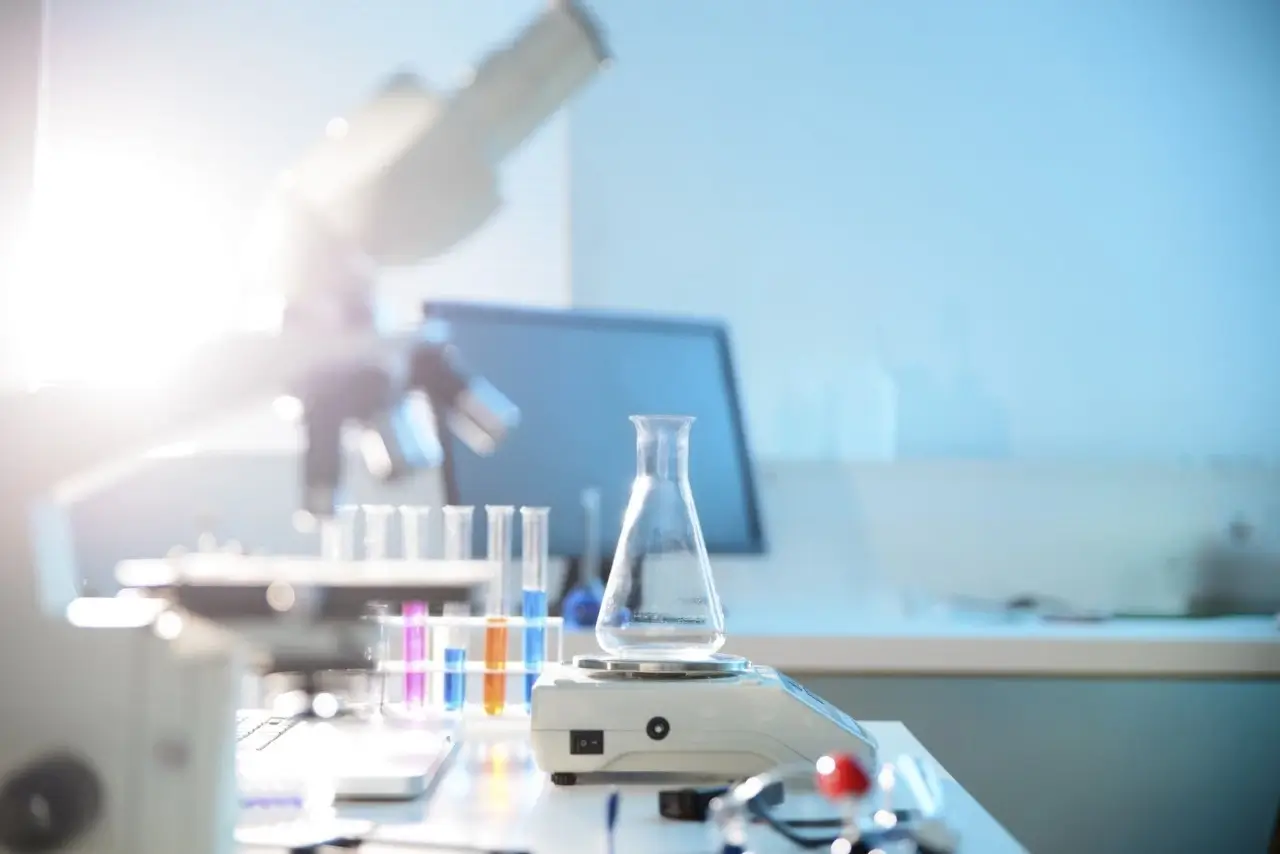 A science lab bench with an Erlenmeyer flask on a digital scale, surrounded by various lab equipment.