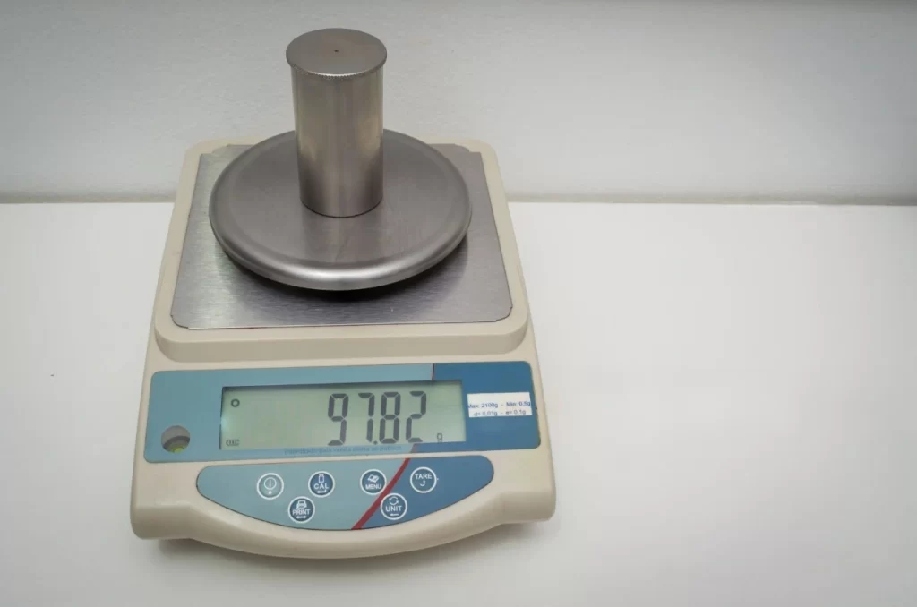 A silver-colored cylindrical weight sitting on a precision digital scale displaying the weight as 97.82 grams.