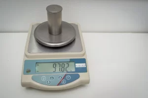A silver-colored cylindrical weight sitting on a precision digital scale displaying the weight as 97.82 grams.