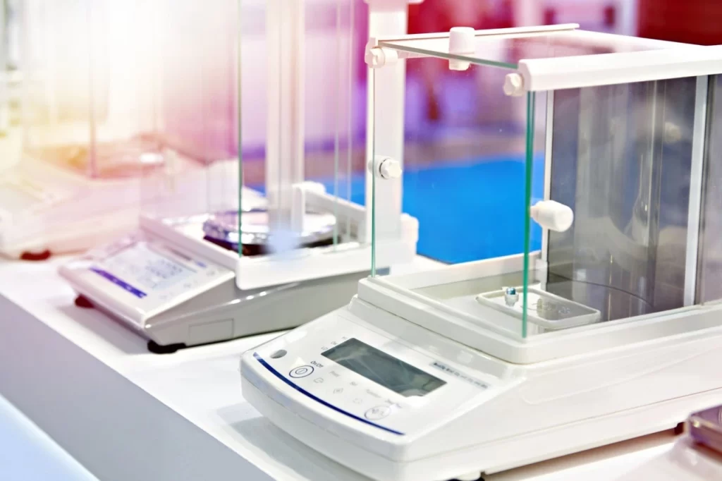 Close-up of modern laboratory analytical and precision electronic balances with glass draft shields on a white lab bench.
