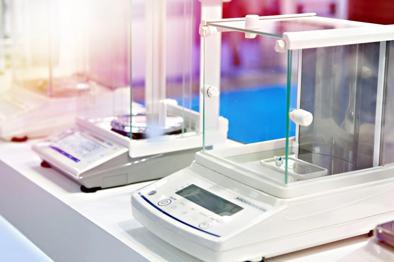 Close-up of modern laboratory analytical and precision electronic balances with glass draft shields on a white lab bench.