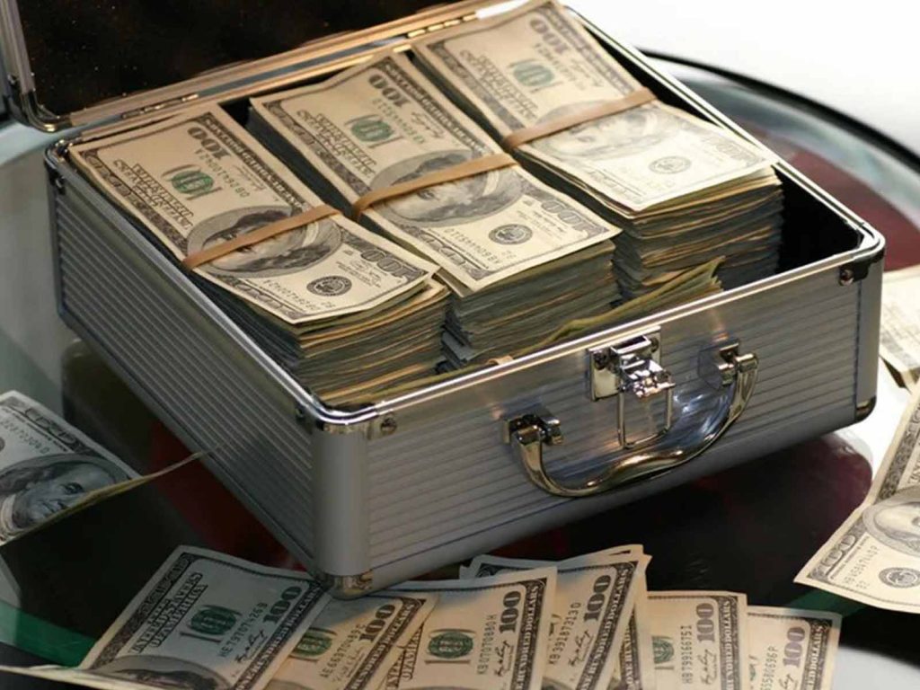 An open silver aluminum briefcase filled with stacks of one hundred US dollar bills bundled with rubber bands.
