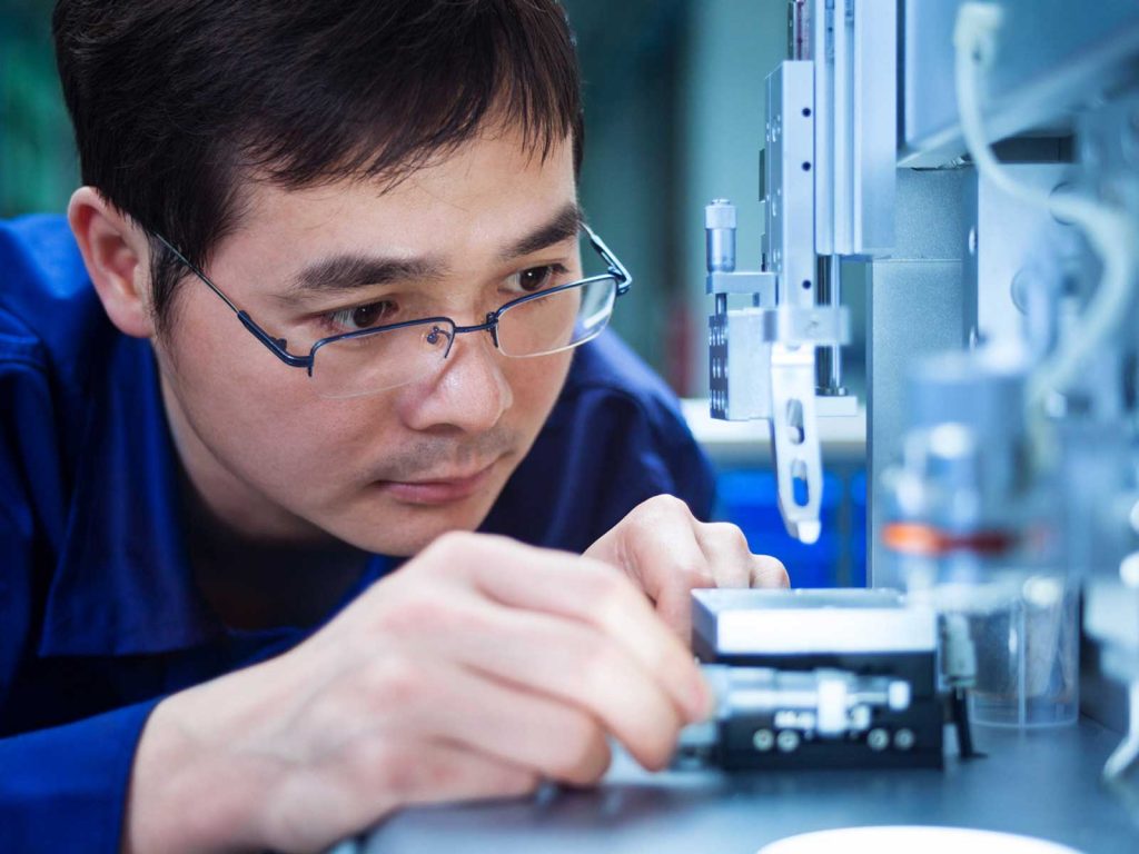 Focused male engineer in a blue uniform closely inspecting and calibrating a piece of precision machinery.