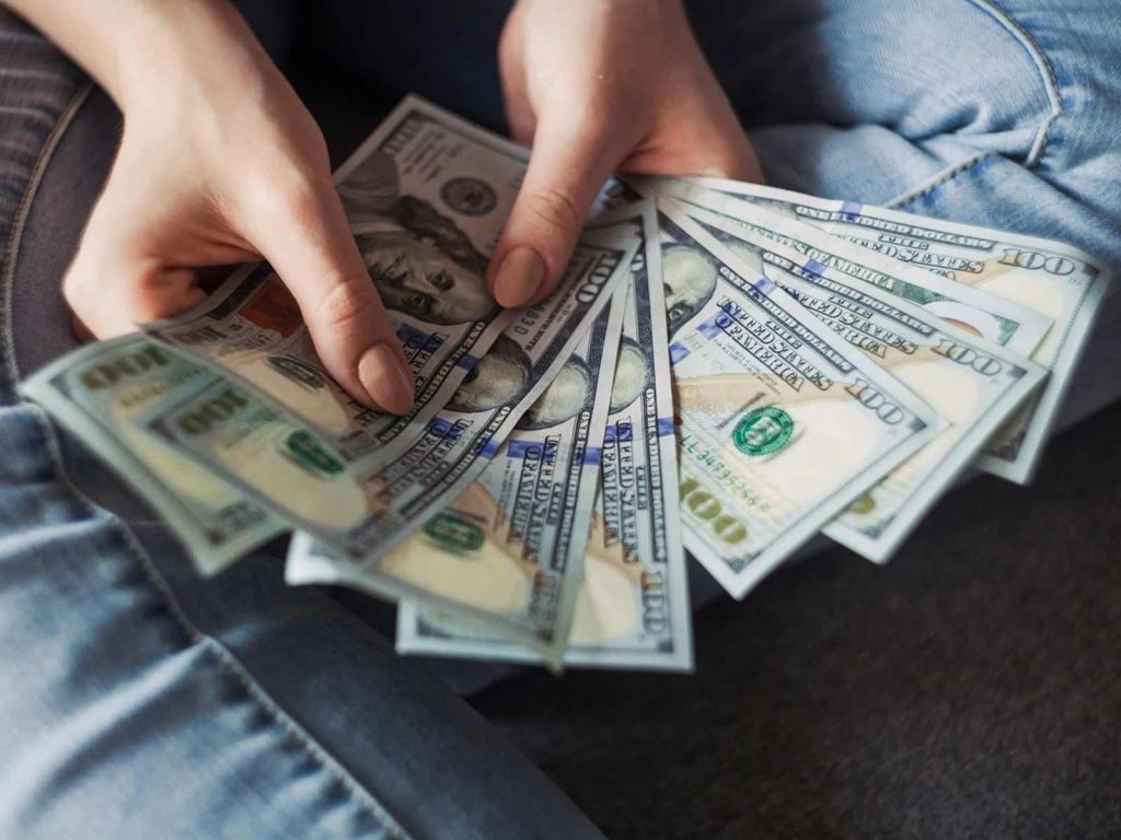 Close-up view of hands holding and counting a fan of US one-hundred dollar bills for laboratory equipment purchase.