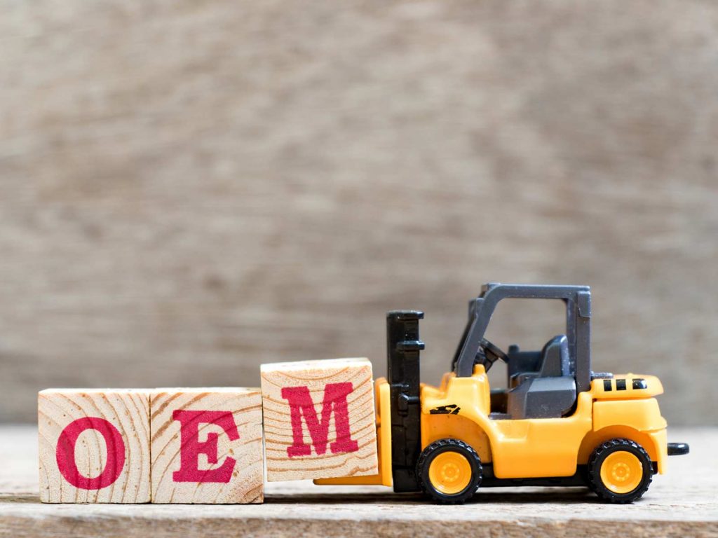 A miniature yellow toy forklift lifting wooden blocks that spell out 'OEM' (Original Equipment Manufacturer).
