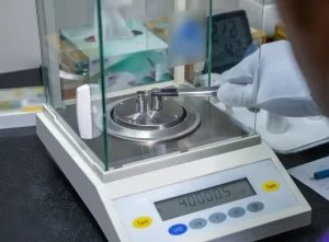 A technician using tweezers to place precision weights on an analytical balance for laboratory calibration.