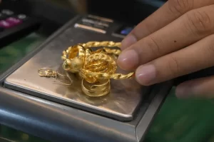 Hand placing gold rings and bracelets on a digital pocket scale for weighing in a jewelry shop environment.