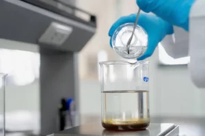 Close-up of a laboratory technician in blue gloves pouring liquid into a glass beaker sitting on a weighing pan.