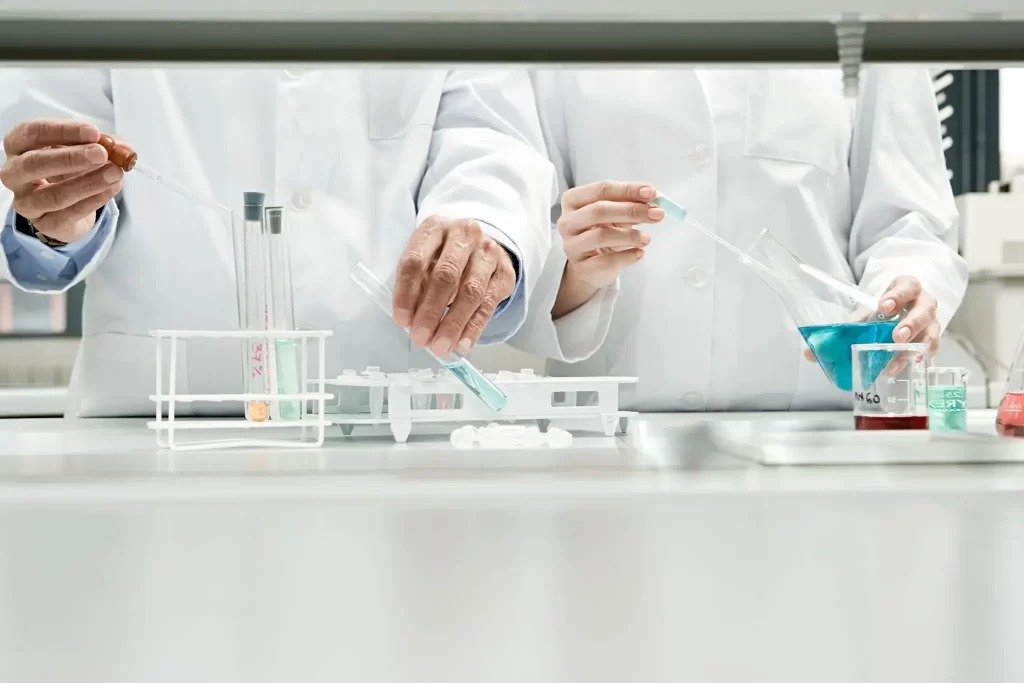Laboratory scientists using pipettes, flasks, and test tubes to handle liquid chemical solutions.