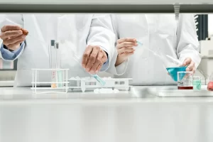 Laboratory scientists using pipettes, flasks, and test tubes to handle liquid chemical solutions.