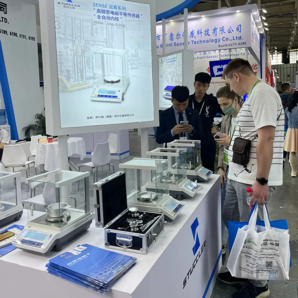 Overseas buyer inspecting Stuccler analytical balance at exhibition booth.