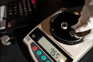 A gloved hand placing diamond rings onto the stainless steel pan of a precision digital jewelry scale.