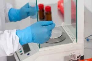 Laboratory technician wearing blue gloves handling an analytical balance draft shield door