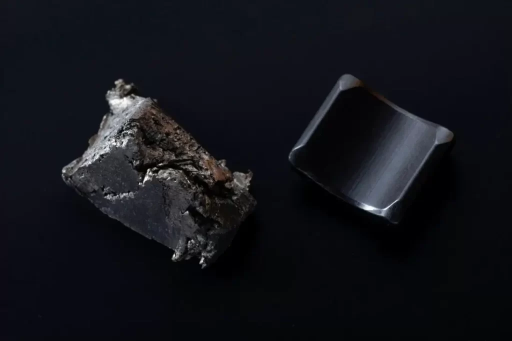 A raw magnetic mineral chunk next to a polished curved permanent magnet on a dark surface.